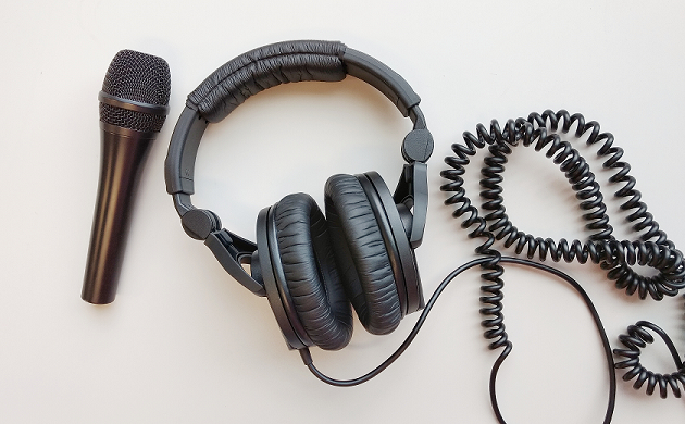 Headphones and a microphone lie on a table, next the jumbled headphone extension cord.